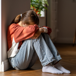 Child sitting on floor with head on their knees