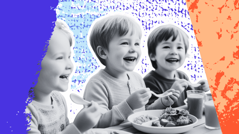 Three young children smiling and eating a meal together at a table, enjoying food in a relaxed, positive environment.